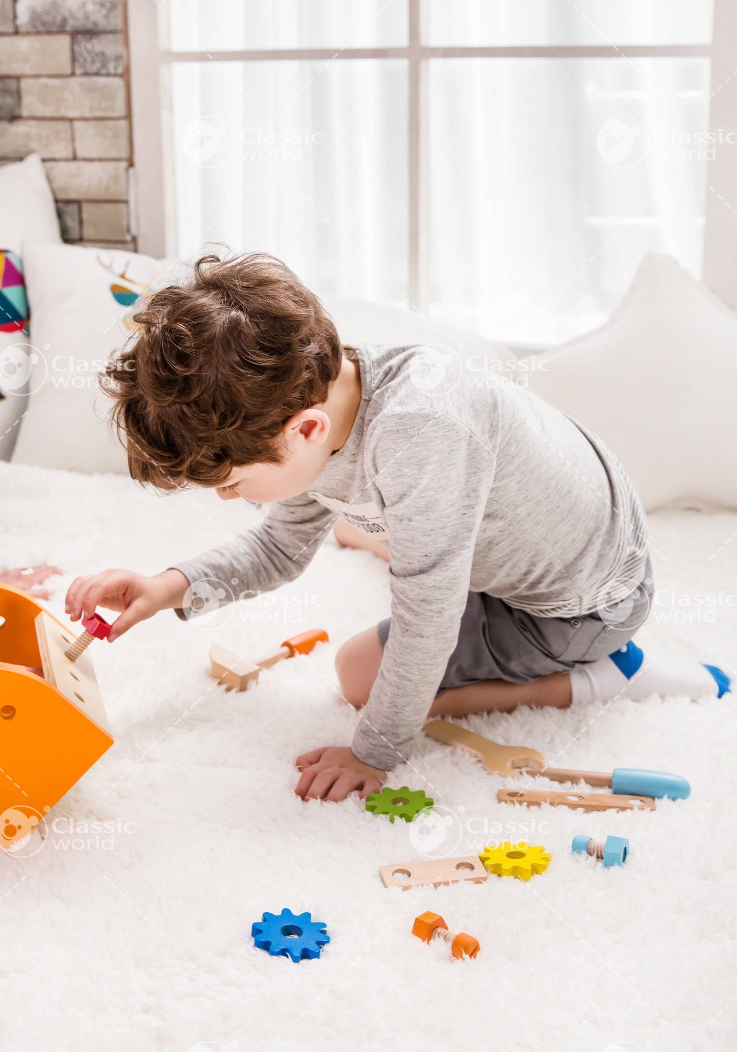 Toddler on model playing with wooden tool pieces and construction set on white carpet in bright room