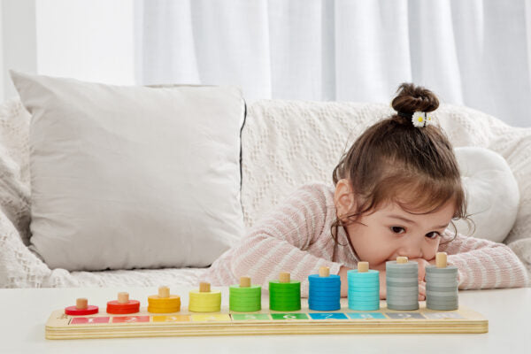 Child on model playing with colorful wooden ring stacker toy on white surface, with stacked rings in rainbow order