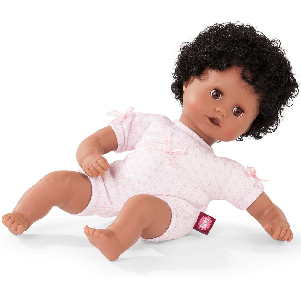 Baby doll with dark curly hair and brown eyes wearing a pink patterned outfit, crawling pose on white background