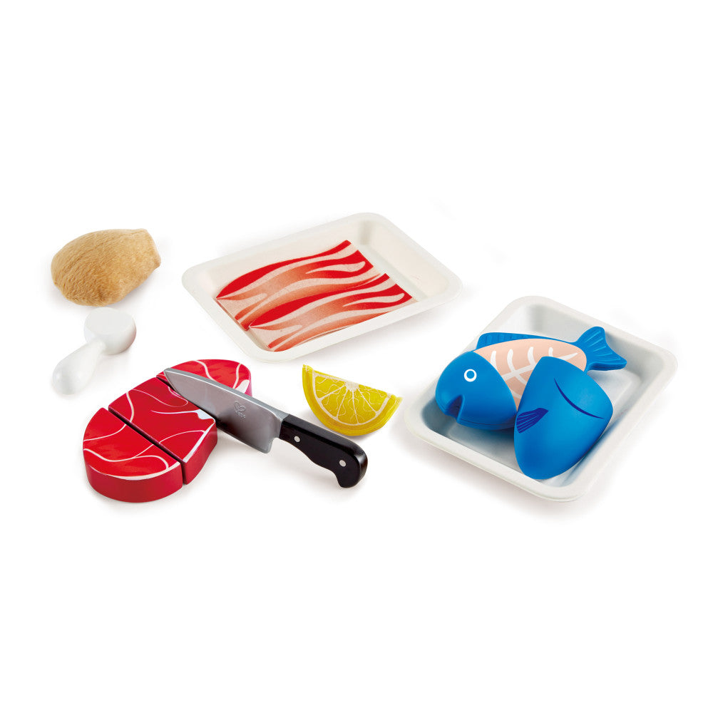 Wooden kitchen playset with red steak, blue fish, sliced bacon, lemon wedge, knife, salt and pepper shakers on white background