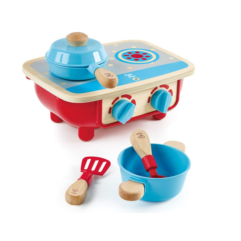 Wooden toddler kitchen playset with blue and red stove, cooktop with burner controls, blue pot with lid and wooden spoon, blue bowl with spoon, and red spatula