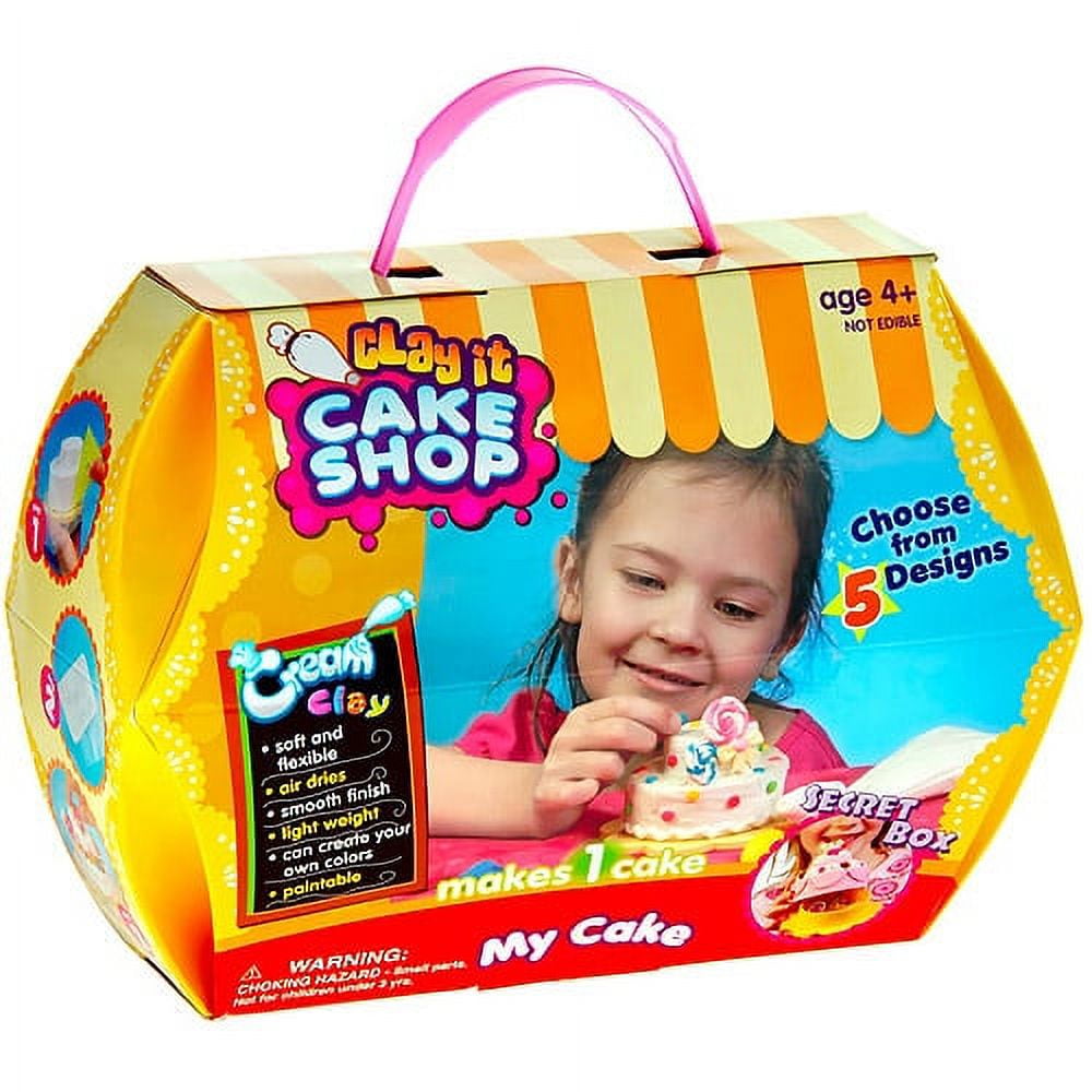 Play It Cake Shop packaging with pink handle, modeled by a child holding a decorative cake, yellow and orange striped awning design, includes cream clay and fiv