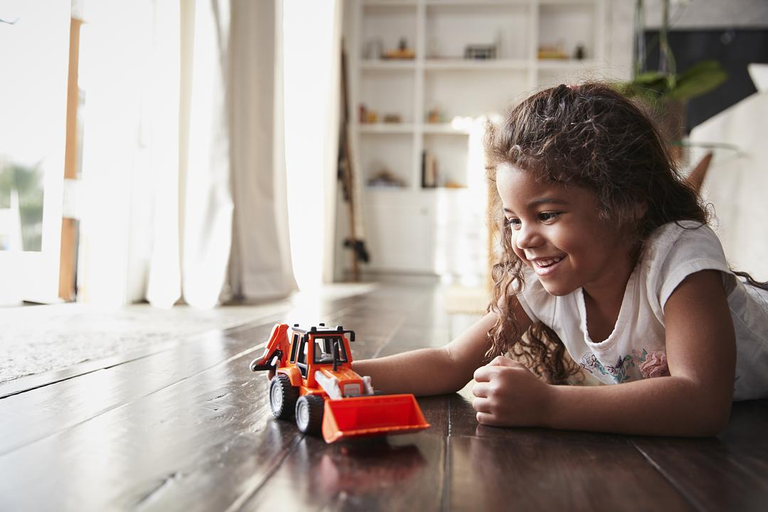 Child on model playing with a red toy construction vehicle on a wooden floor indoors