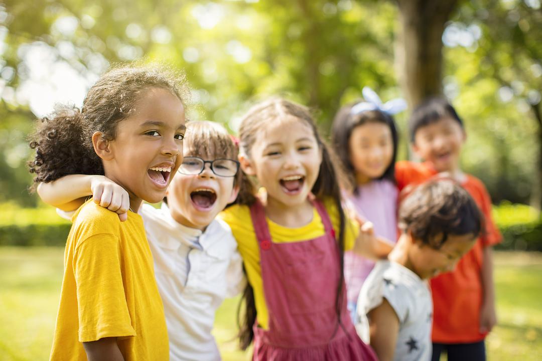 Group of children laughing and playing together outdoors in a sunny park setting