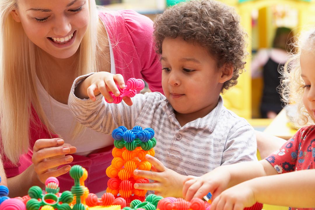 Adult and children playing with colorful stacking toy rings at a table, modeled by a child
