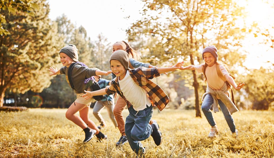 Group of children running and playing together in a sunny autumn park with golden fall foliage