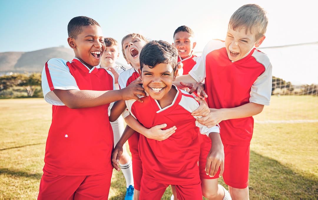 Group of children in red and white sports uniforms celebrating together on a sunny outdoor field