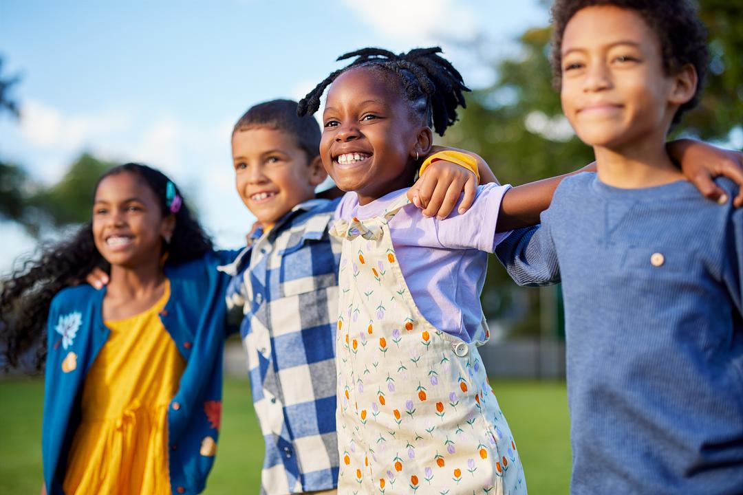 Group of children smiling and hugging outdoors on a sunny day in a grass field