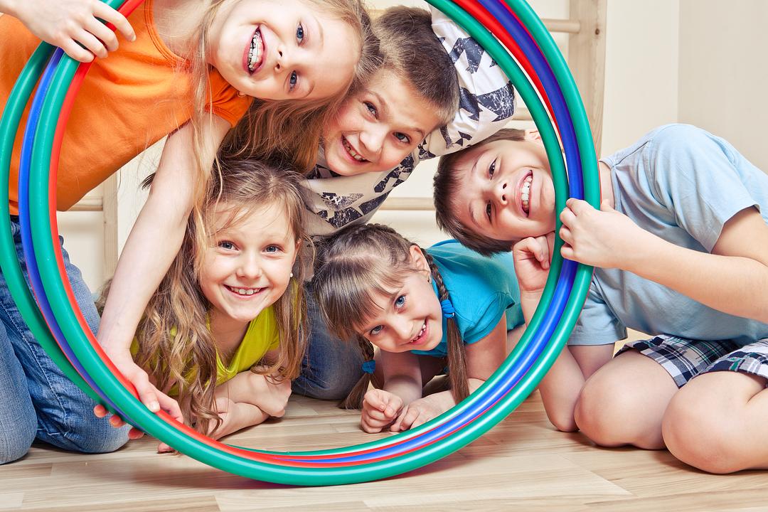 Group of children playing together with a colorful hula hoop on a wooden floor, smiling and laughing
