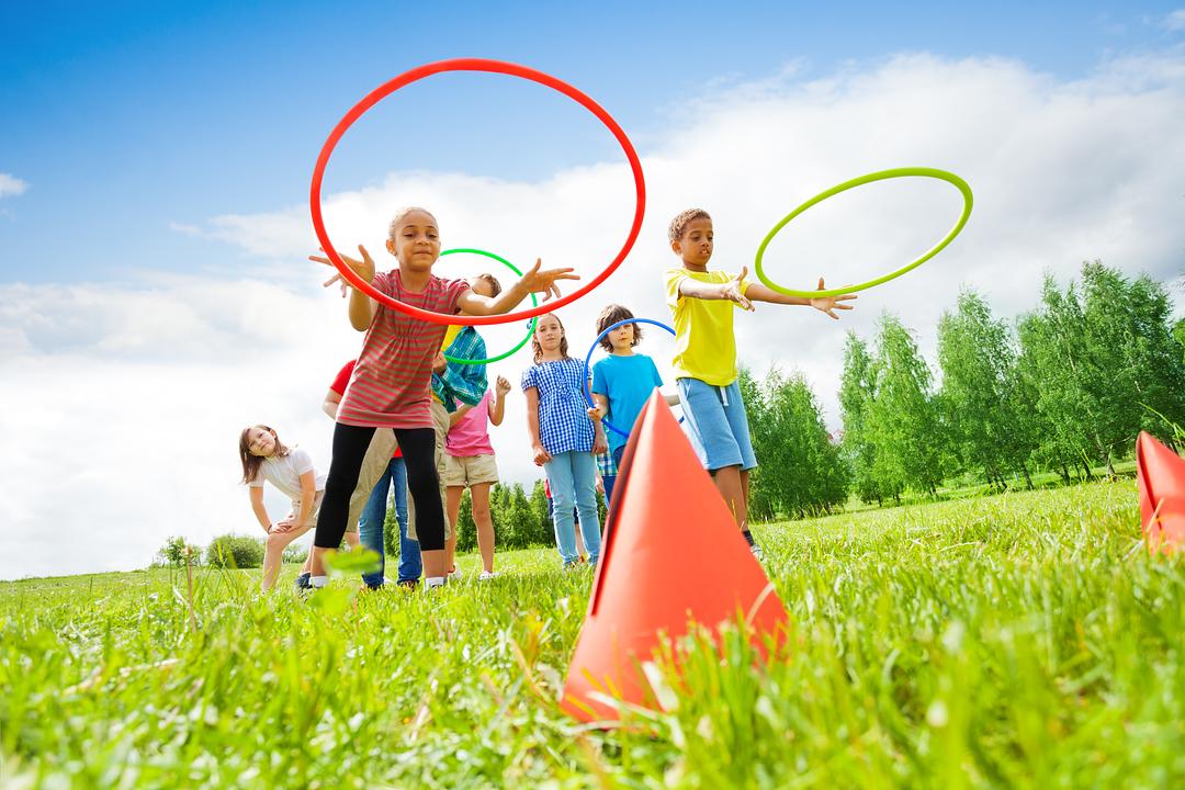 Children playing outdoors in a grassy field with hula hoops and colorful cones on a sunny day