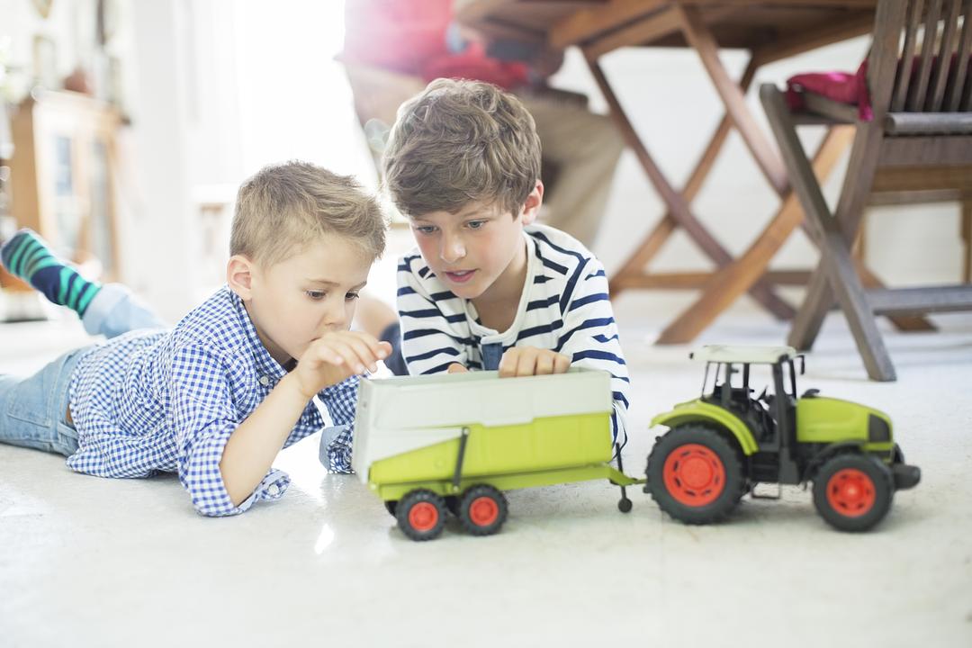 Two boys playing with toy farm vehicles on the floor, modeled by children in a home setting