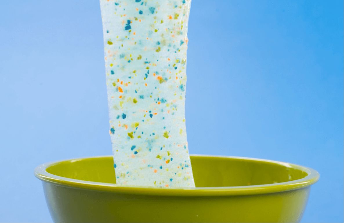 White slime with colorful confetti-like specks stretched above a lime green bowl against a blue background