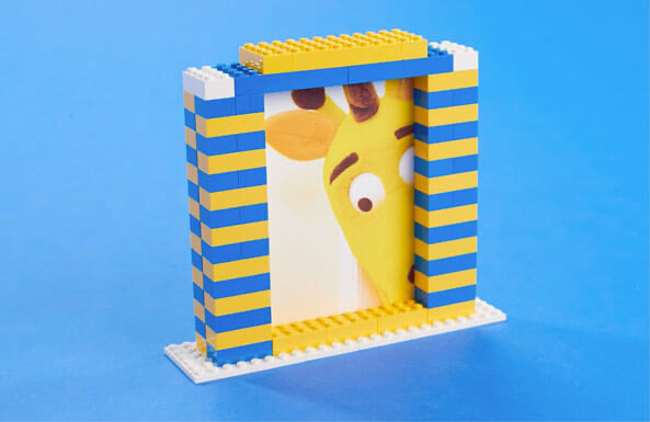 LEGO photo frame with blue and yellow striped walls and a yellow smiley face design on plain blue background