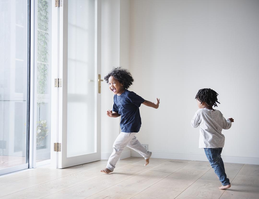 Two children playing and running indoors in a bright, modern room with white walls and large glass doors