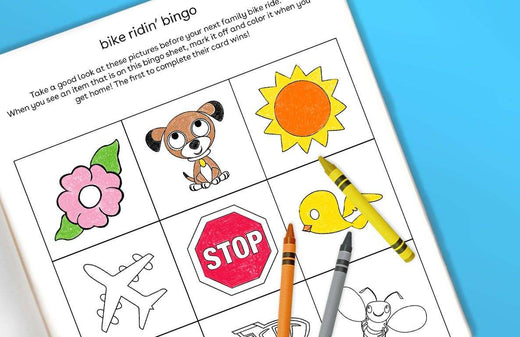Bike Ridin' Bingo printable game sheet with illustrated squares featuring a flower, puppy, sun, bird, stop sign, airplane, and crayons on a blue background