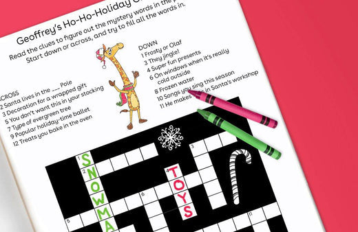 Printed holiday crossword puzzle featuring Geoffrey the giraffe with a pink and green crayon on a bright pink background