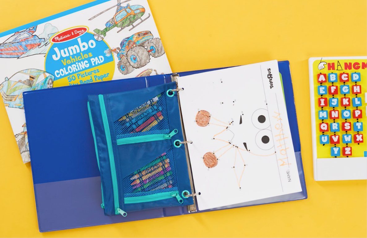 Overhead flat lay of children's travel activities on yellow background, including open blue organizer with mesh pockets containing colored pencils, a Melissa &