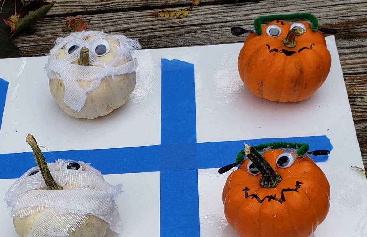 DIY Halloween tic-tac-toe game with white wrapped mummy pumpkins and orange monster pumpkins on a board with blue grid lines