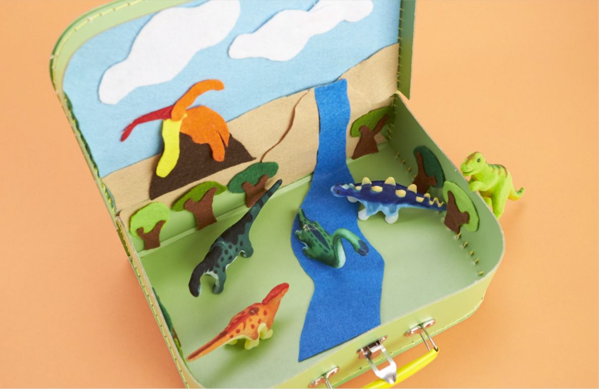 Dinosaur-themed fabric travel case with colorful felt dinosaurs, volcano, river, and landscape scenes on light green exterior