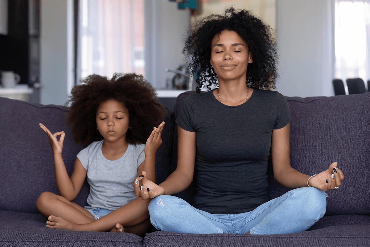 Adult and child sitting together on a couch with eyes closed, hands in meditation pose
