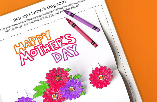 Pop-up Mother's Day card printable with colorful flowers and 'Happy Mother's Day' text, shown with purple and pink crayons on orange background