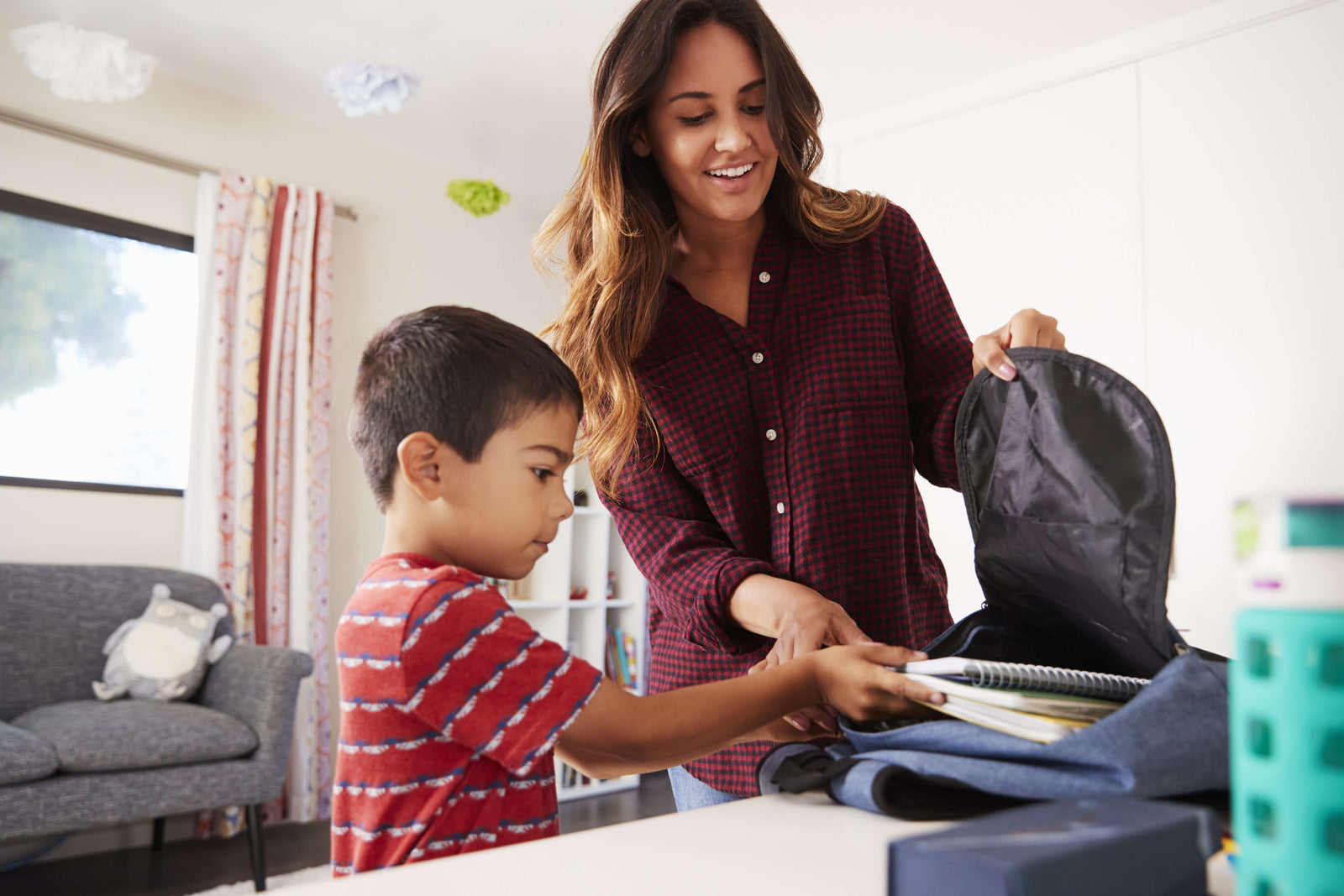 Woman and child packing a backpack together at a table, preparing school supplies for the next day