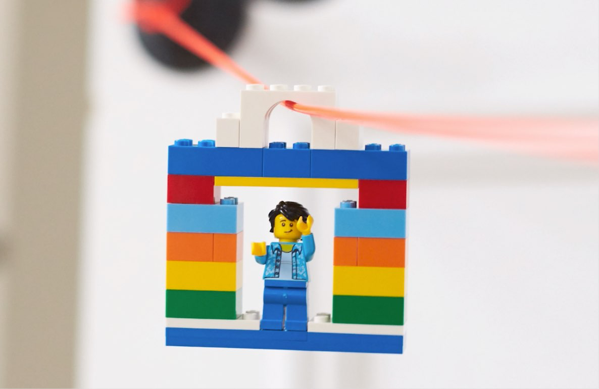 LEGO minifigure in blue outfit on colorful brick structure with orange zipline cord attached above