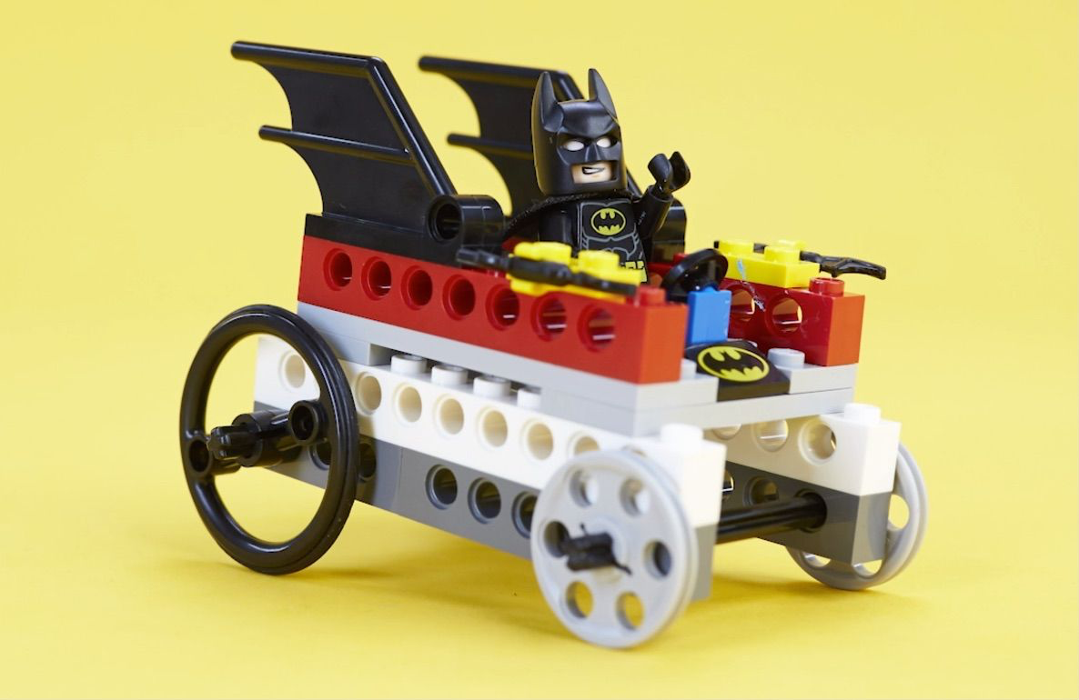 LEGO Batman minifigure in a buildable vehicle with black wings, red and white base, yellow accents, and white wheels on yellow background