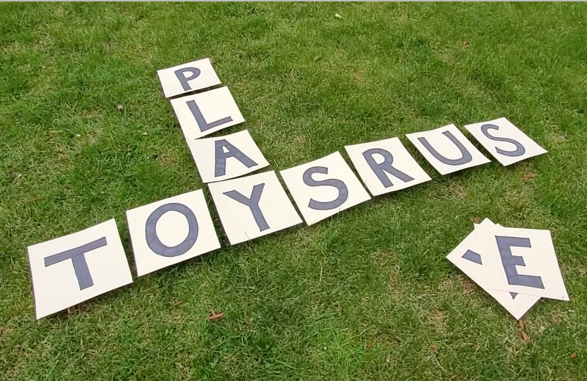 PLAY SAURUS crossword puzzle spelled out with letter tiles on grass