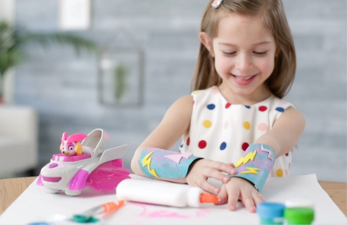 Child modeled by a girl wearing colorful PAW Patrol superhero cuffs on her wrists while crafting at a table with art supplies