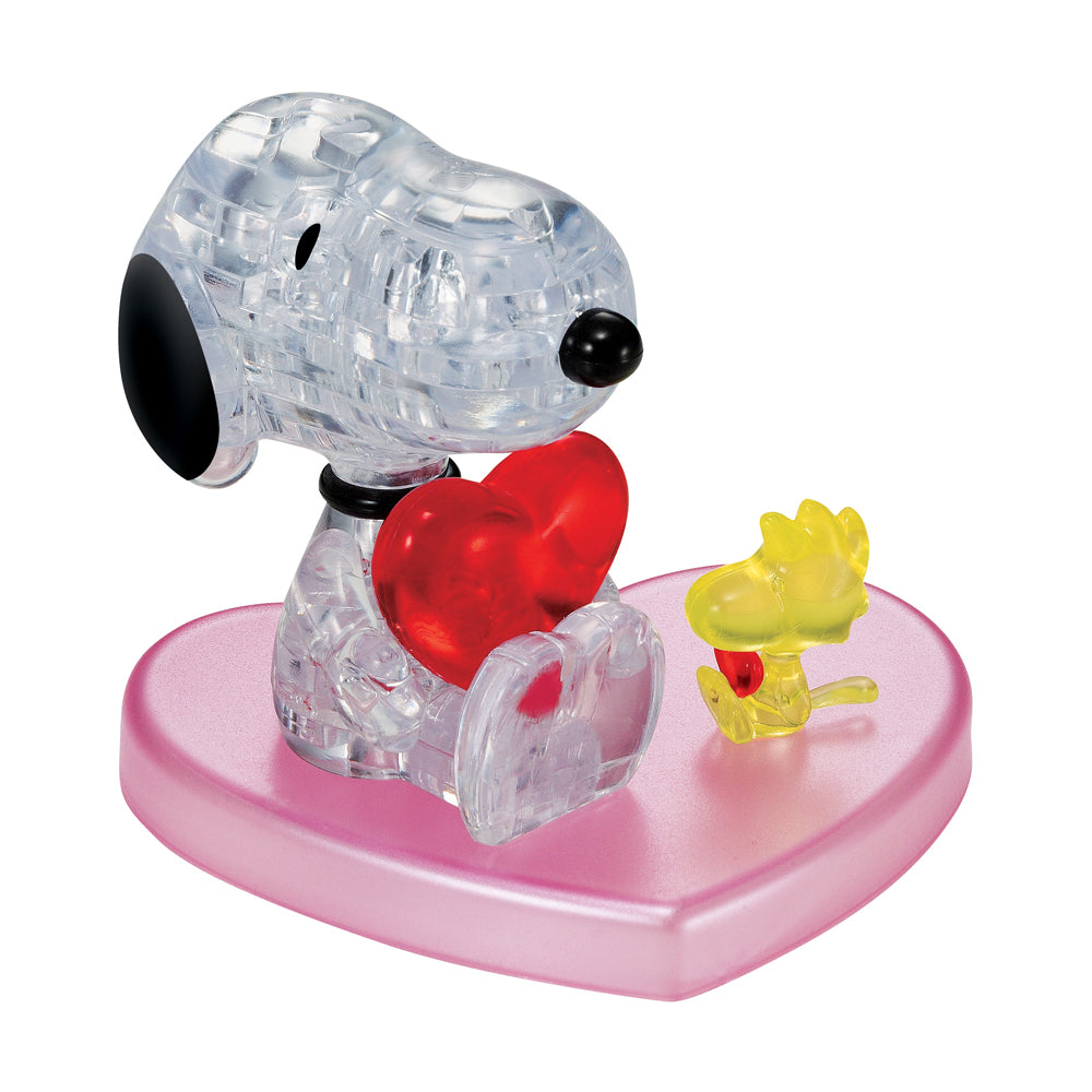 Clear plastic 3D crystal puzzle of Snoopy holding a red heart on a pink heart-shaped base, with a small yellow Woodstock figure