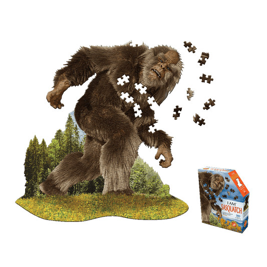 Madd Capp I AM SASQUATCH 300-piece jigsaw puzzle showing a large furry brown sasquatch figure in a forest landscape with puzzle pieces scattered, displayed with