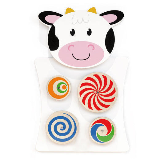 Cow-shaped activity wall panel with five spinning disc toys in colorful patterns including orange, red and white swirl, blue spiral, and multicolor designs