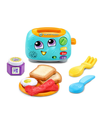 LeapFrog Yum-2-3 Toaster turquoise learning toy with purple eyes and orange handle, shown with colorful play food pieces including bread, bacon, egg, and utensi