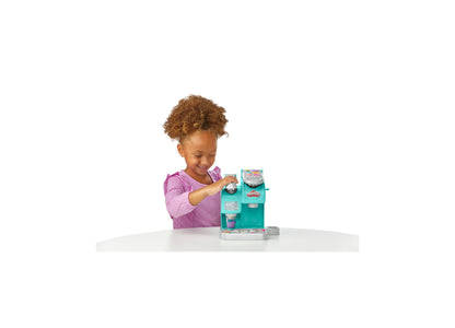 Child in pink shirt playing with Play-Doh Kitchen Creations Colorful Cafe turquoise playset on white table
