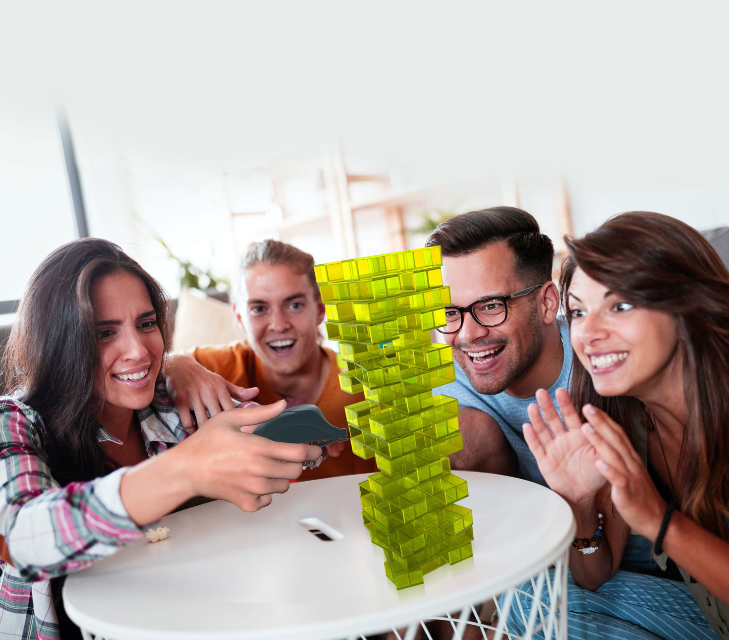 Four adults playing Fotorama Trembling Tower Precision Block Game, smiling as they carefully remove and stack neon yellow blocks on a white table
