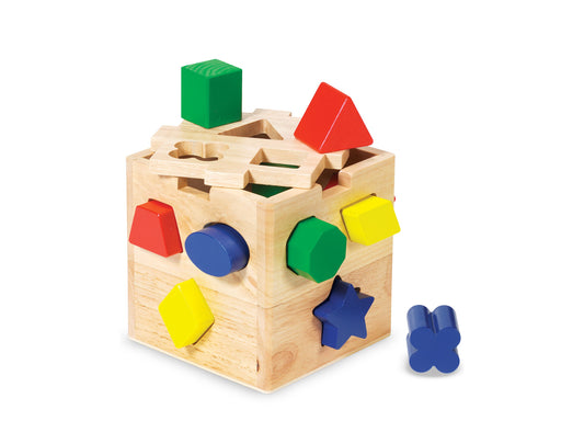 Wooden shape-sorting cube with colorful blocks: red trapezoid, yellow square, blue circle, green pentagon, and blue star shape; includes removable pieces on top