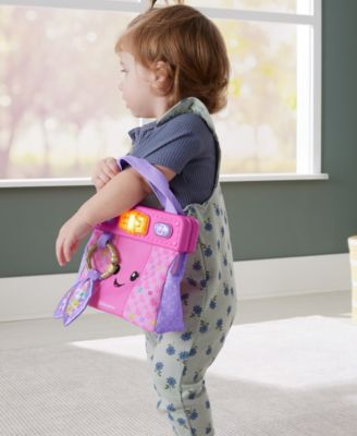 Fisher-Price Laugh & Learn On-the-Go Learning Purse in pink with interactive accessories, held by child