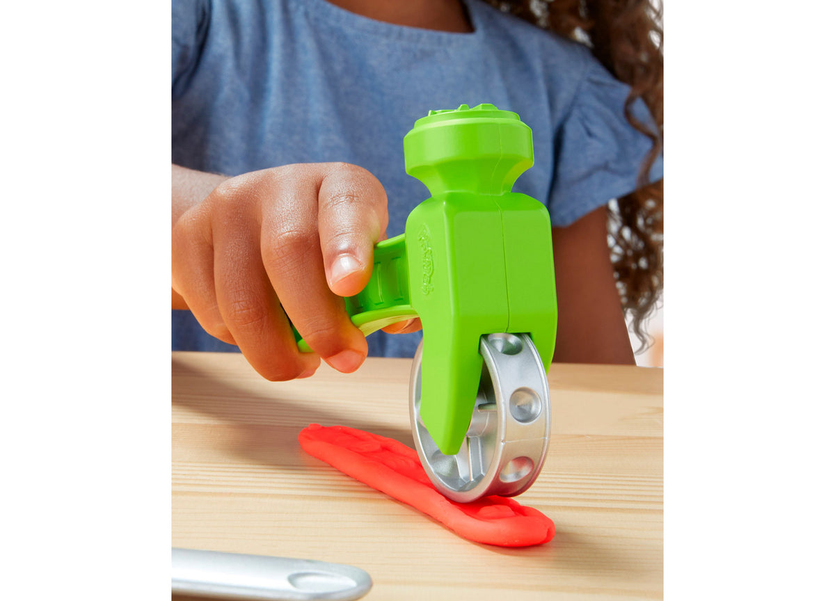 Child's hand holding green Play-Doh Stamp N Saw Tool with red Play-Doh on a surface