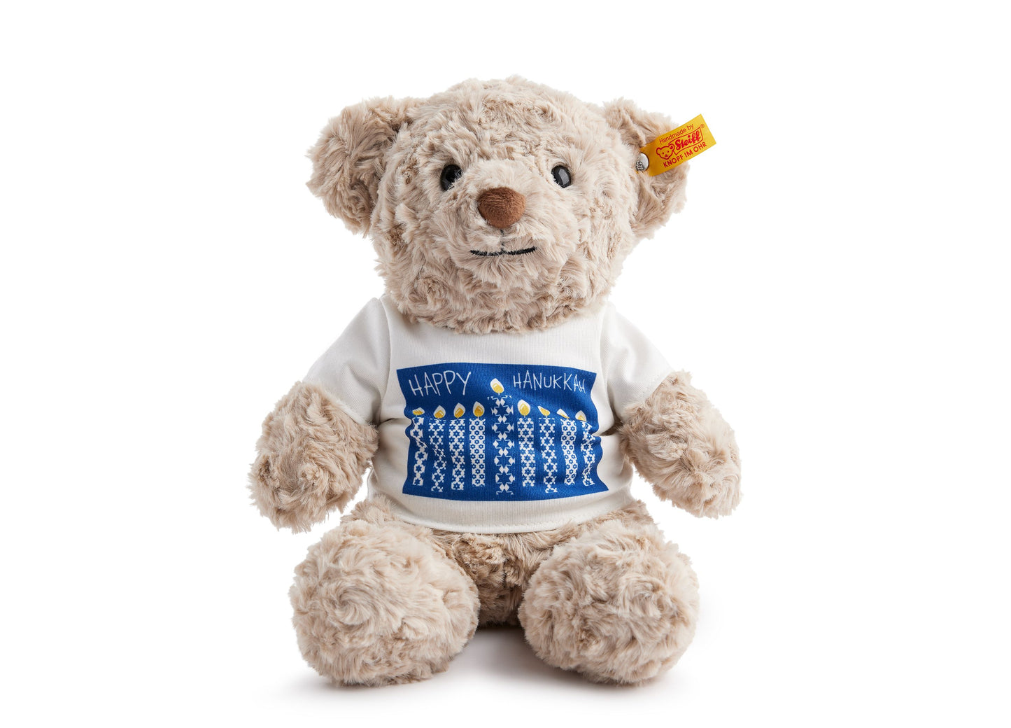 Cream-colored plush teddy bear wearing white sweater with blue Happy Hanukkah design and menorah pattern, Steiff yellow tag on ear