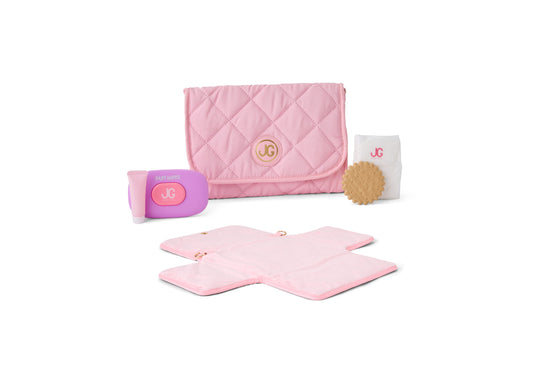 Pink quilted doll diaper bag with JG logo, includes baby wipes container, diaper changing pad, and tan textured accessory