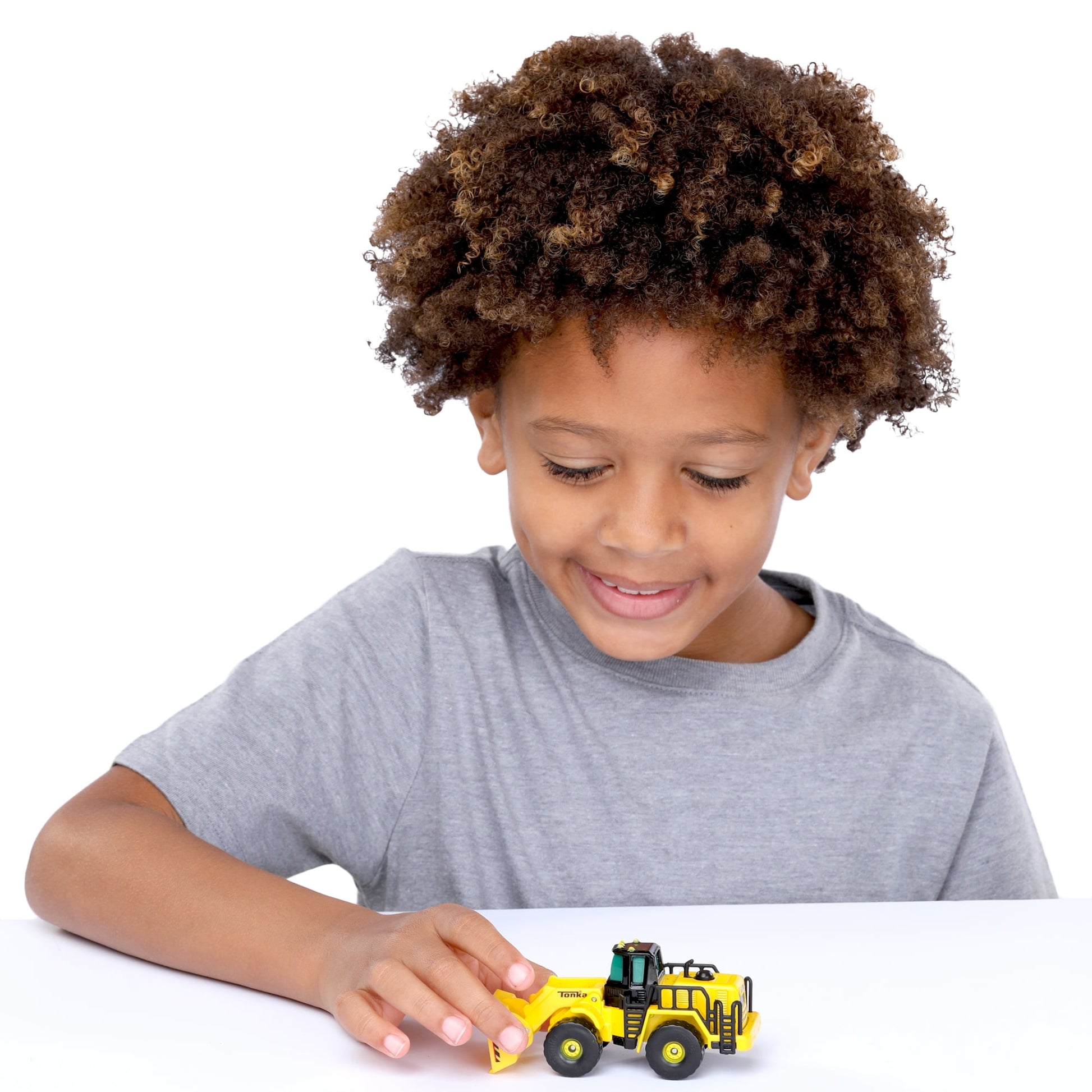 Child modeled by a child playing with yellow Tonka metal front loader toy on white surface