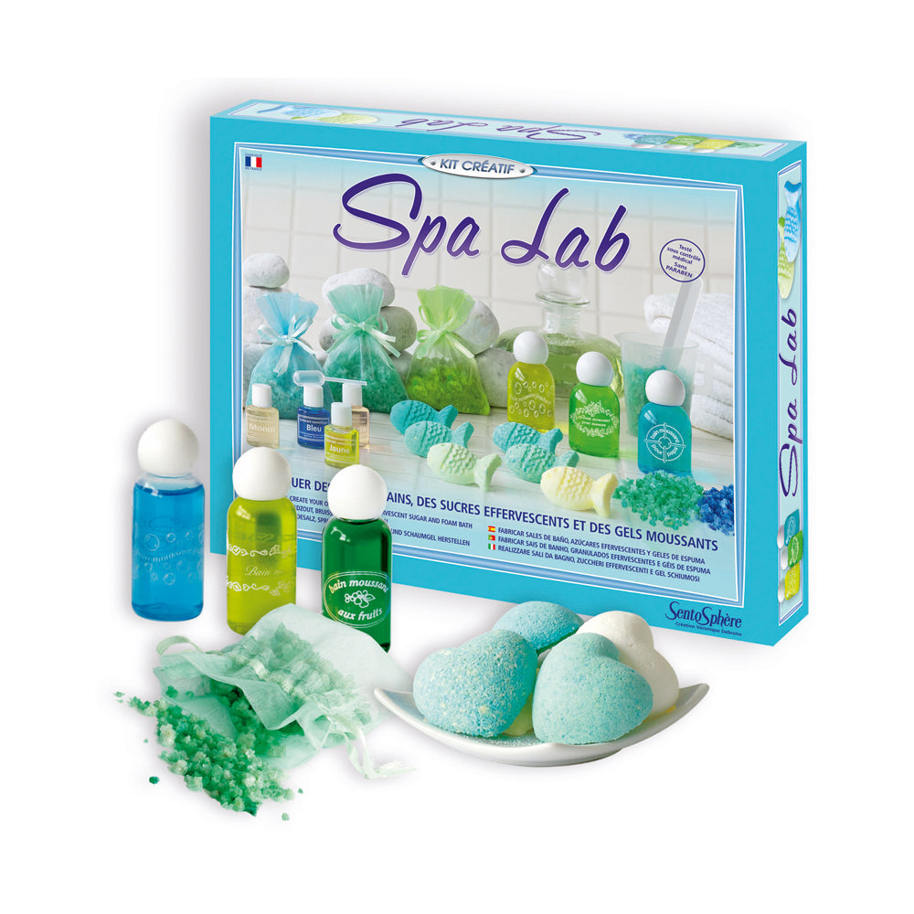 Spa Lab kit with turquoise box, three colored liquid bottles, bath bomb bath balls on white plate, green bath salts in mesh bags, and white towels