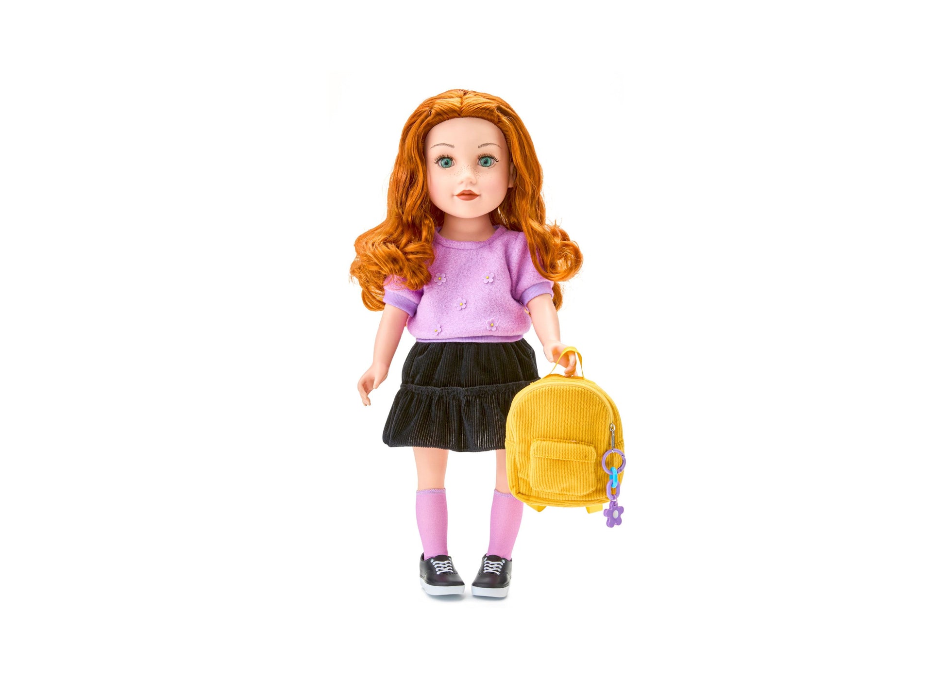 Journey Girls 18 inch doll with orange wavy hair, wearing lavender top, black pleated skirt, pink socks, and black sneakers, holding yellow backpack with purple