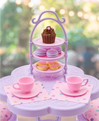 Purple toy tea set with tiered stand, pink teacups, saucers, macarons, and cupcake on display table