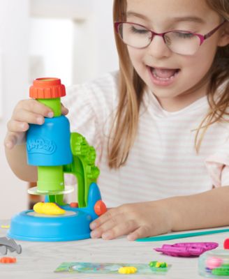 Girl with glasses playing with Play-Doh Light and Look Microscope Playset, stacking blue, green, and red components