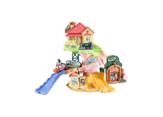 VTech Bluey Road Trip Interactive Playset featuring a yellow cottage with red roof, blue slide, yellow spiral slide, brown tree house, pink arch bridge, and red
