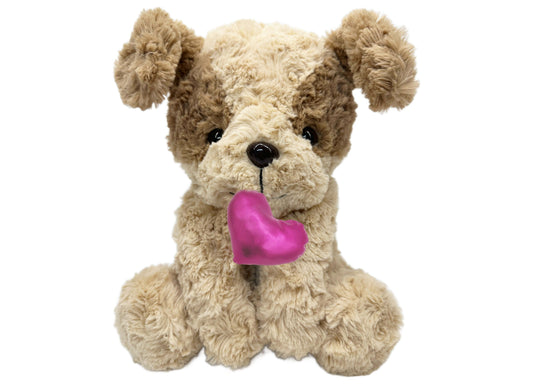 Cream and tan plush puppy with floppy ears holding a bright pink heart toy in its mouth