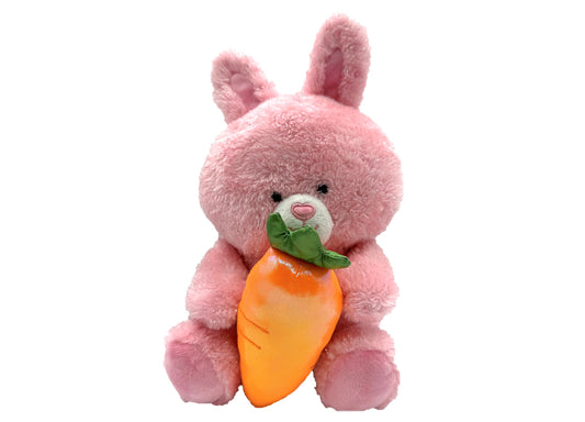 Pink plush bunny with long ears holding an orange carrot with green leaves