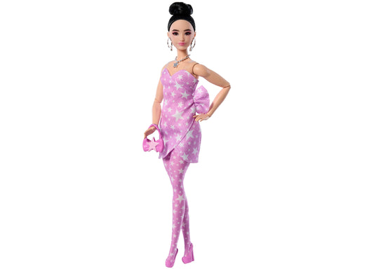 Barbie doll wearing pink star-print dress with matching tights and star-shaped purse, black hair in top bun, silver necklace and hoop earrings, posed against wh